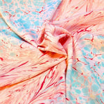 Close-up of marbled fabric with pink, red, and light blue swirl patterns, smoothly folded